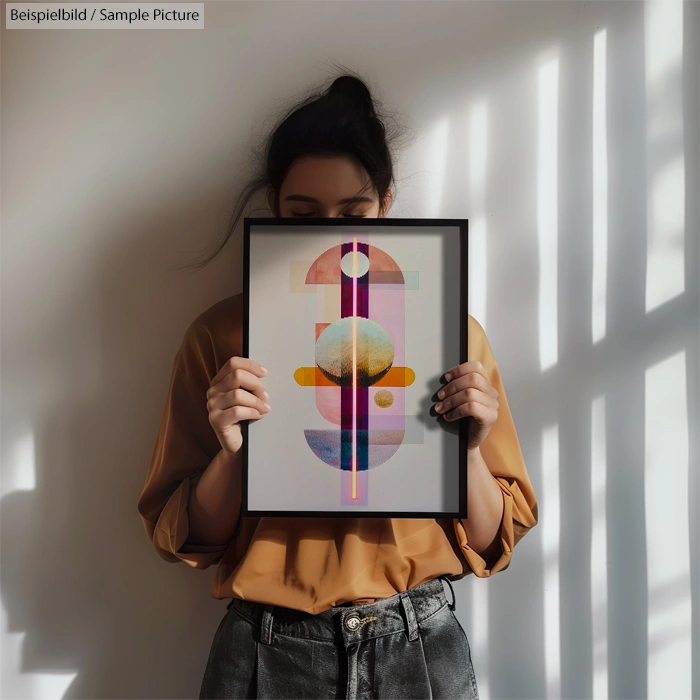 Person holding abstract geometric artwork with circles and lines, casting a shadow on white wall behind.