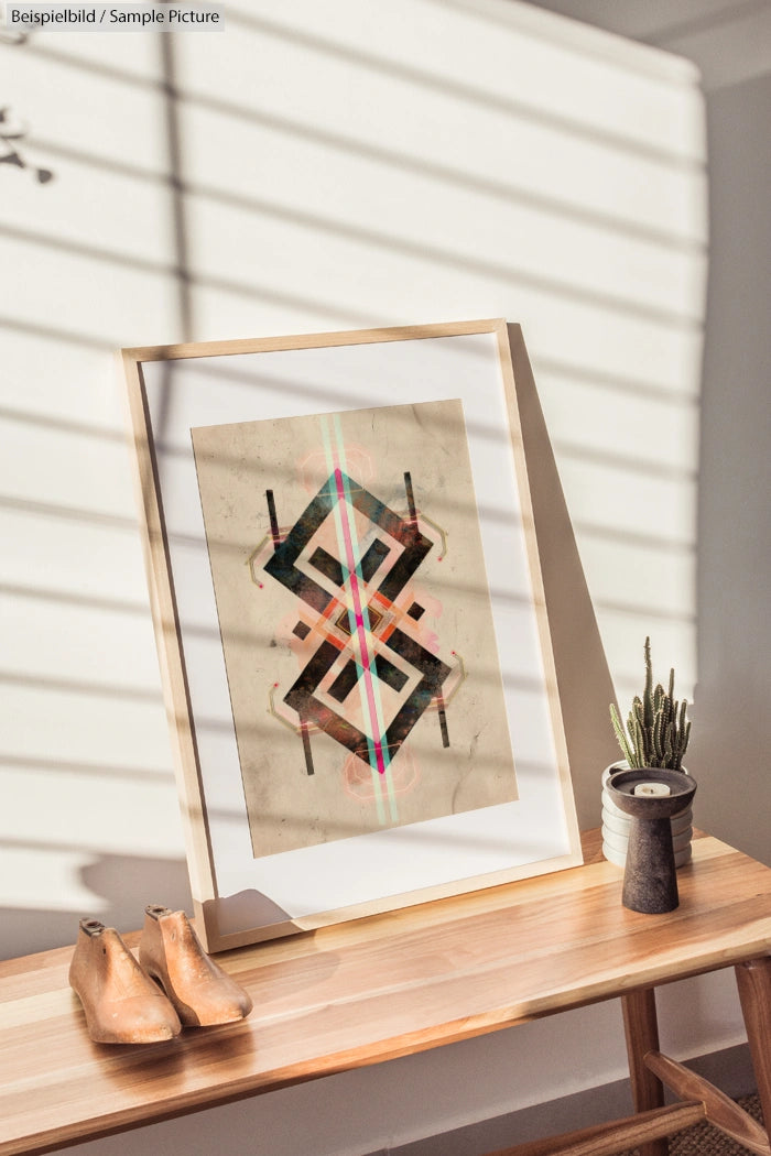 Framed abstract geometric art on a wooden bench, with a small cactus and shoes nearby, sunlight casting shadows.