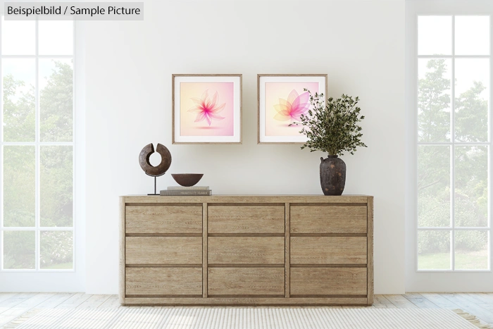 Minimalist room with wooden dresser, two floral paintings, and potted plant, framed by large windows and white walls.