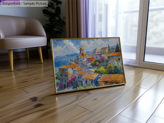 Framed painting of a Mediterranean village with colorful rooftops and hillside, leaning on a wooden floor in a modern room.