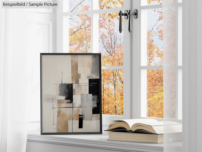 Abstract painting beside books on windowsill with fall trees visible outside.