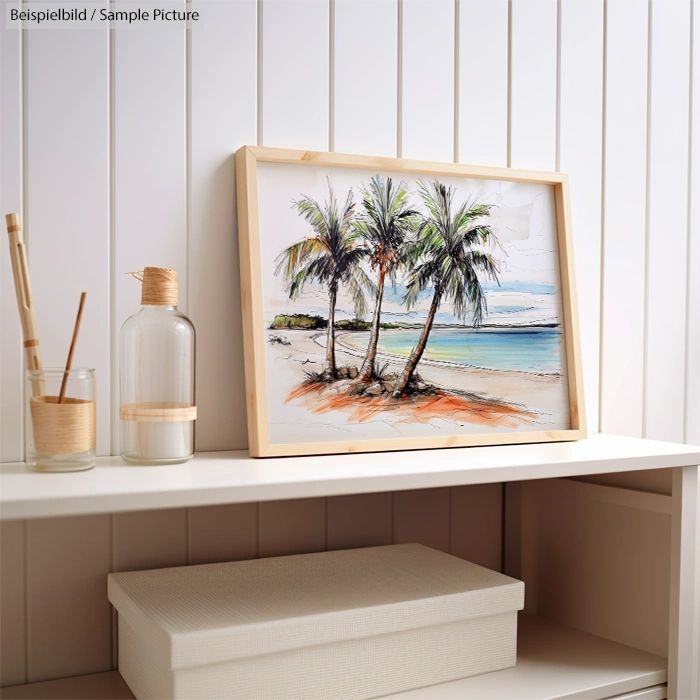 Framed beach painting with palm trees on a shelf next to a glass bottle and box, set against a white paneled wall.