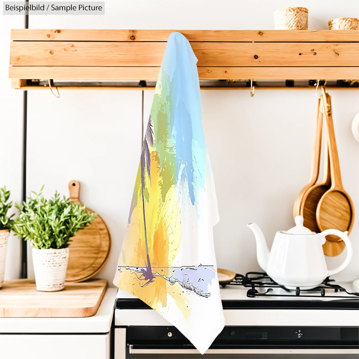 Kitchen towel with abstract palm tree design hanging above stove near plants and teapot.