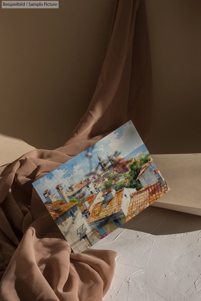 Postcard with European cityscape above beige fabric backdrop, displaying rooftops and a distant dome.