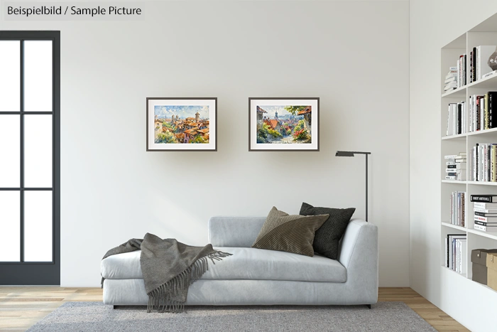 Modern living room with a gray sofa, two framed landscape paintings on wall, and a tall lamp next to shelves with books.
