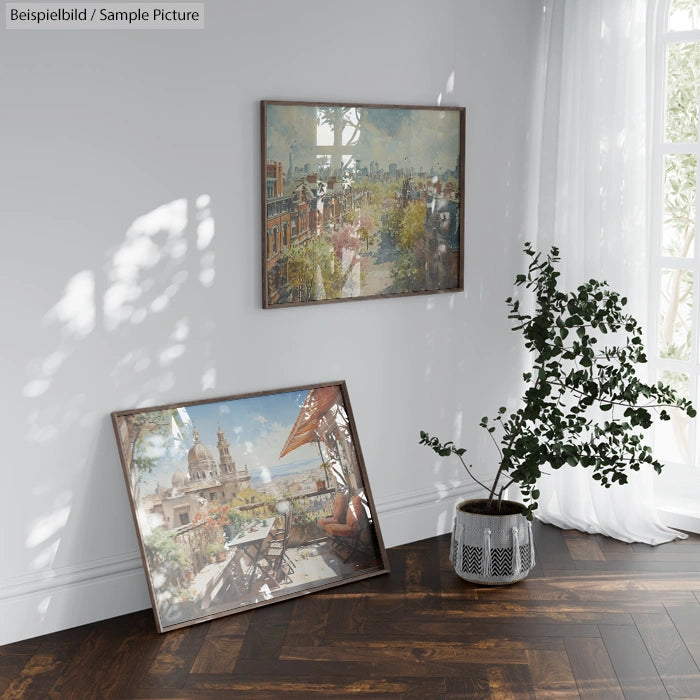 Two framed paintings displayed on the floor and wall near a potted plant in a sunlit room with wooden flooring.