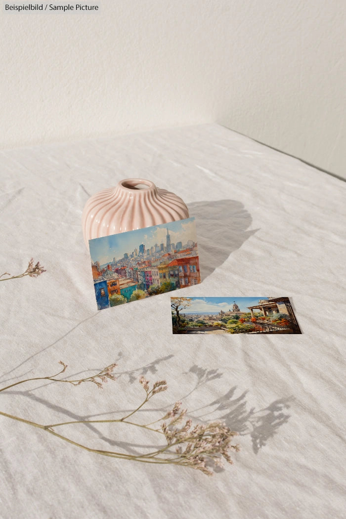 Painted postcards on white fabric with dried flowers and pink ceramic vase.
