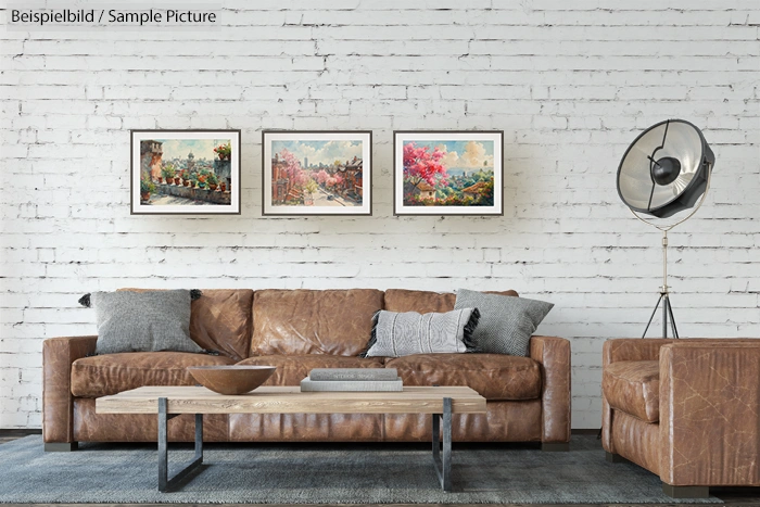 Stylish living room with brown leather sofa, modern coffee table, and three framed paintings on a white brick wall.