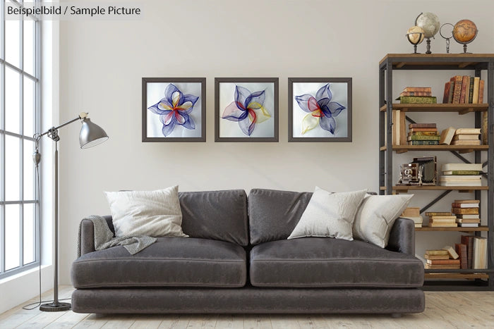 Modern living room with a gray sofa, pillows, three abstract flower paintings, and a bookshelf with books and a globe.