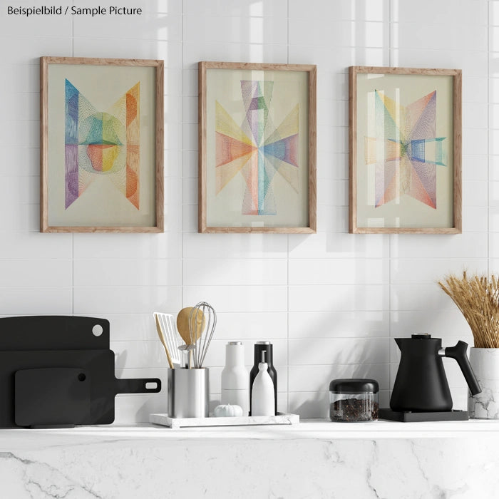 Modern kitchen countertop with black utensils and vases, against white tile wall displaying abstract art in wooden frames.
