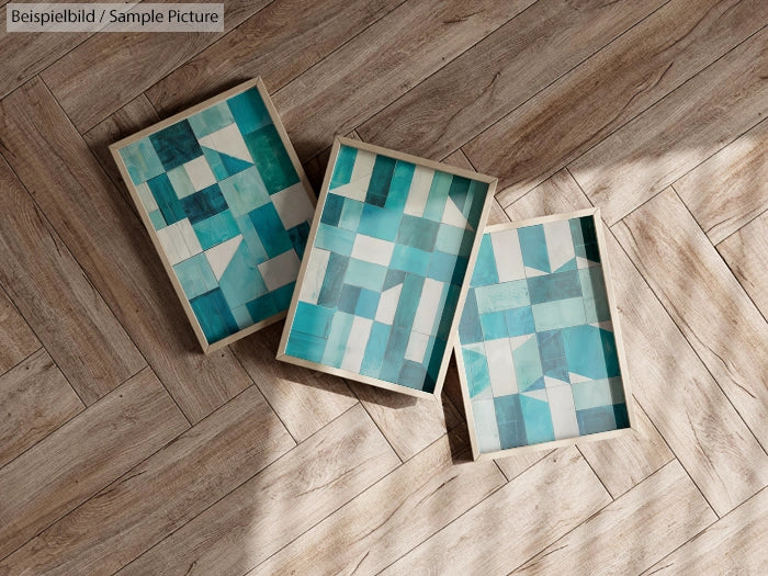 Three framed geometrical teal art pieces on wooden herringbone floor.
