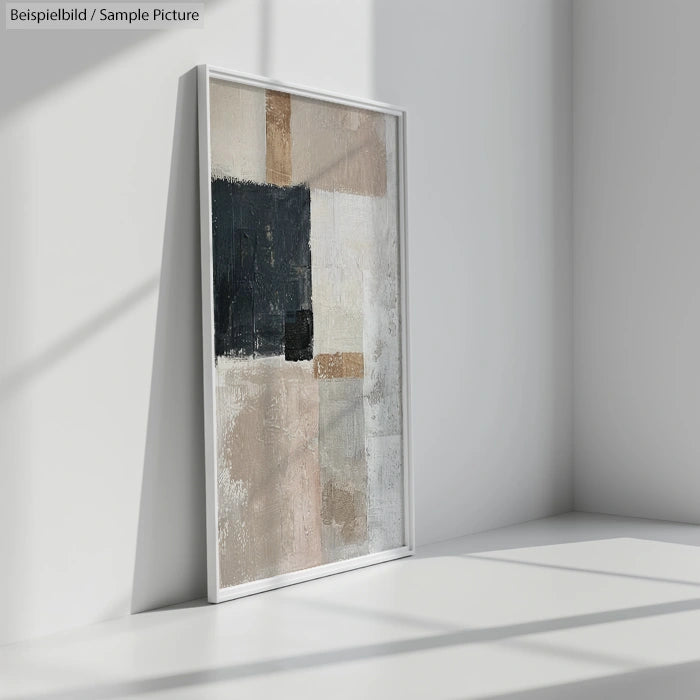 Framed abstract painting with geometric shapes in beige, black, and white on a sunlit wall.